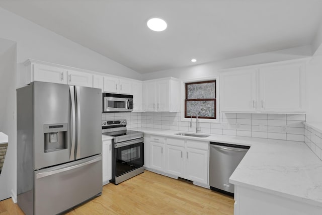 kitchen with decorative backsplash, appliances with stainless steel finishes, vaulted ceiling, sink, and white cabinets