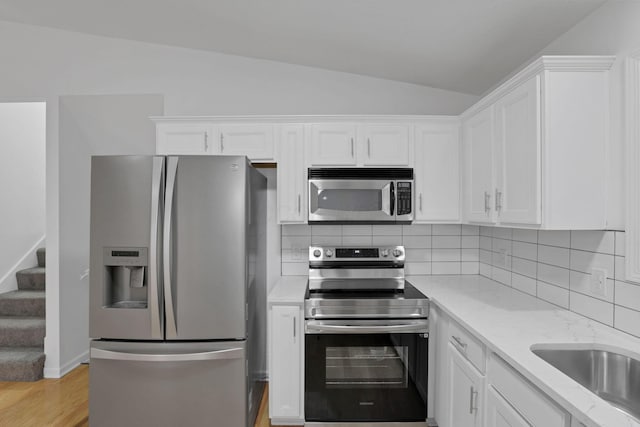 kitchen featuring appliances with stainless steel finishes, white cabinetry, and lofted ceiling