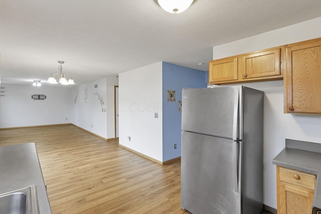 kitchen featuring stainless steel fridge, sink, decorative light fixtures, light hardwood / wood-style flooring, and a chandelier