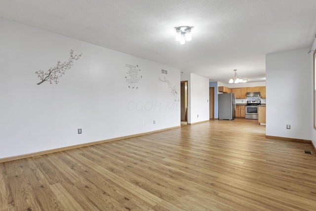 unfurnished living room featuring light hardwood / wood-style floors, a textured ceiling, and an inviting chandelier