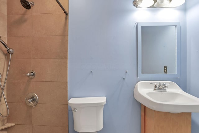 bathroom with a tile shower, toilet, and sink