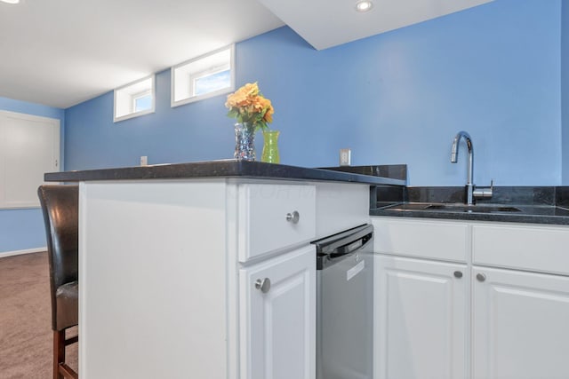 kitchen featuring kitchen peninsula, stainless steel dishwasher, sink, white cabinets, and carpet floors