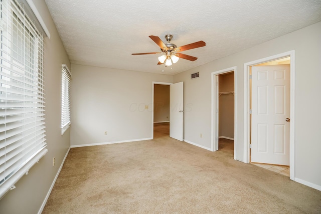 unfurnished bedroom with a spacious closet, light colored carpet, a textured ceiling, a closet, and ceiling fan