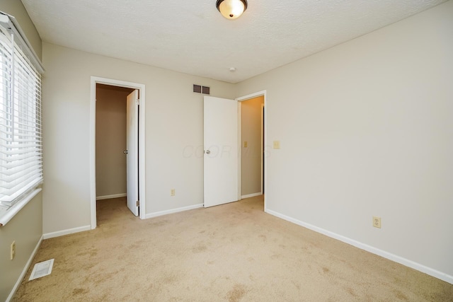 unfurnished bedroom with a closet, a walk in closet, light colored carpet, and a textured ceiling