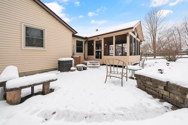 snow covered back of property featuring central AC and a sunroom