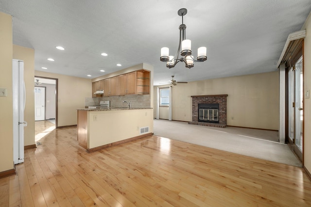 kitchen featuring white refrigerator, stove, a brick fireplace, hanging light fixtures, and light stone countertops