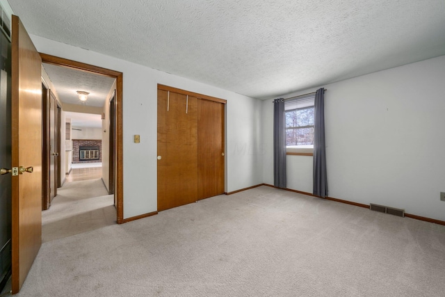 unfurnished bedroom featuring a brick fireplace, a closet, a textured ceiling, and light colored carpet