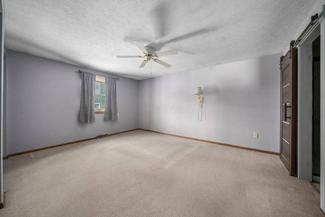 carpeted empty room with ceiling fan, a barn door, and a textured ceiling