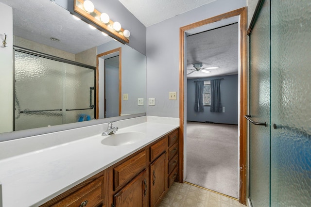 bathroom with ceiling fan, vanity, an enclosed shower, and a textured ceiling