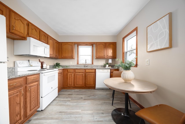 kitchen with light stone counters, white appliances, sink, and light hardwood / wood-style flooring