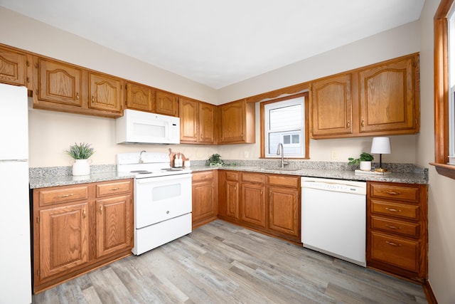 kitchen with light stone countertops, light wood-type flooring, white appliances, and sink