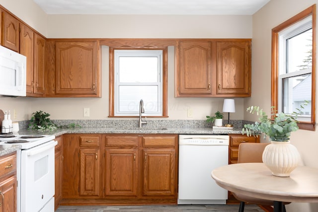 kitchen featuring light stone counters, white appliances, and sink