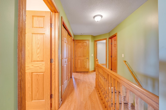 hall with a textured ceiling and light hardwood / wood-style flooring