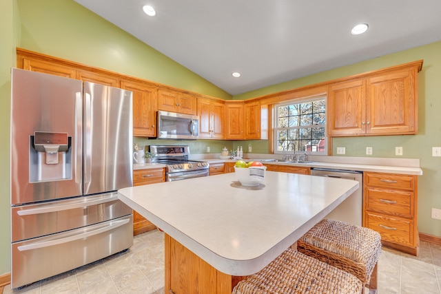 kitchen with a kitchen breakfast bar, stainless steel appliances, vaulted ceiling, sink, and a kitchen island