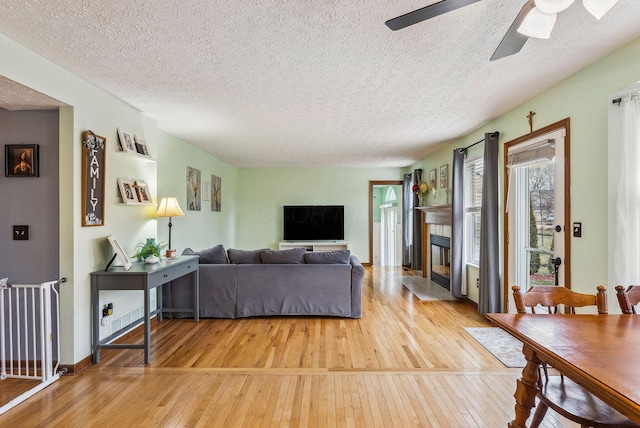 living room featuring hardwood / wood-style flooring, ceiling fan, a tile fireplace, and a textured ceiling