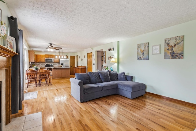 living room featuring ceiling fan, a fireplace, a textured ceiling, and light wood-type flooring