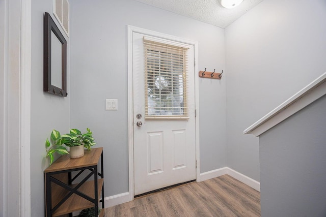 entryway with lofted ceiling, wood-type flooring, and a textured ceiling