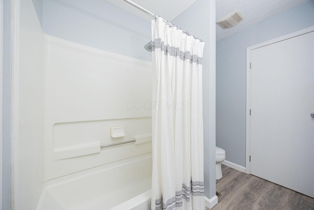 bathroom featuring hardwood / wood-style flooring, shower / bath combination with curtain, toilet, and a textured ceiling