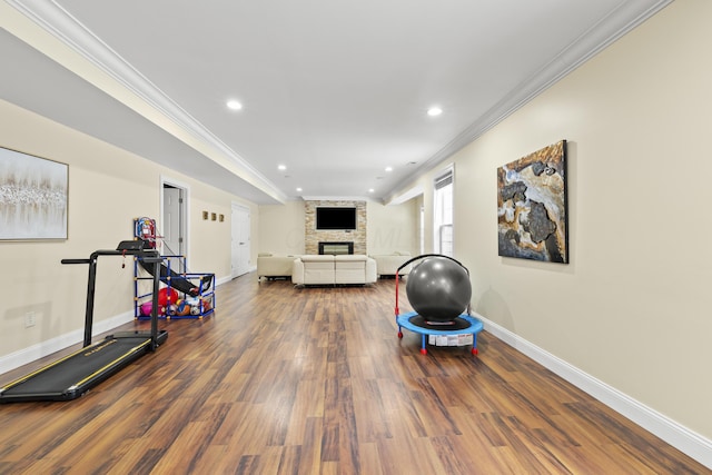 exercise room with ornamental molding, a stone fireplace, and dark wood-type flooring