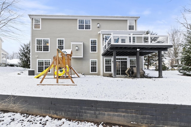 snow covered house with a playground and a wooden deck