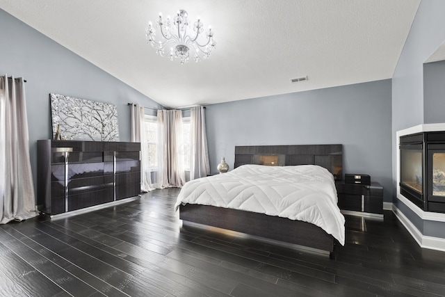 bedroom with dark hardwood / wood-style floors, a multi sided fireplace, lofted ceiling, and a chandelier