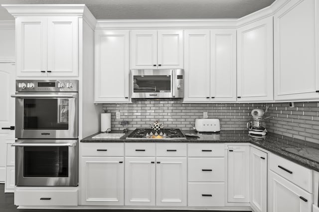 kitchen featuring white cabinetry, crown molding, dark stone counters, decorative backsplash, and appliances with stainless steel finishes