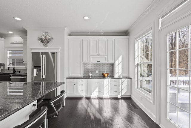 kitchen with backsplash, stainless steel appliances, dark wood-type flooring, dark stone countertops, and white cabinets