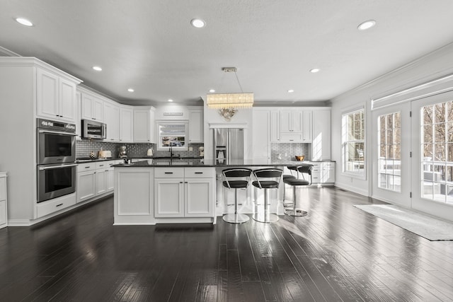 kitchen with appliances with stainless steel finishes, ornamental molding, a kitchen island, white cabinetry, and hanging light fixtures