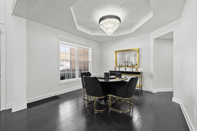 dining area with a raised ceiling, dark hardwood / wood-style flooring, and a notable chandelier