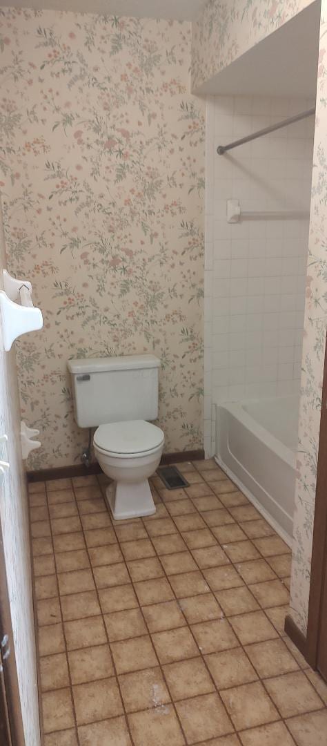 bathroom with tile patterned flooring, tiled shower / bath, and toilet