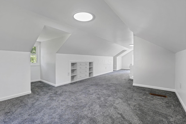 additional living space with dark colored carpet, built in shelves, and lofted ceiling