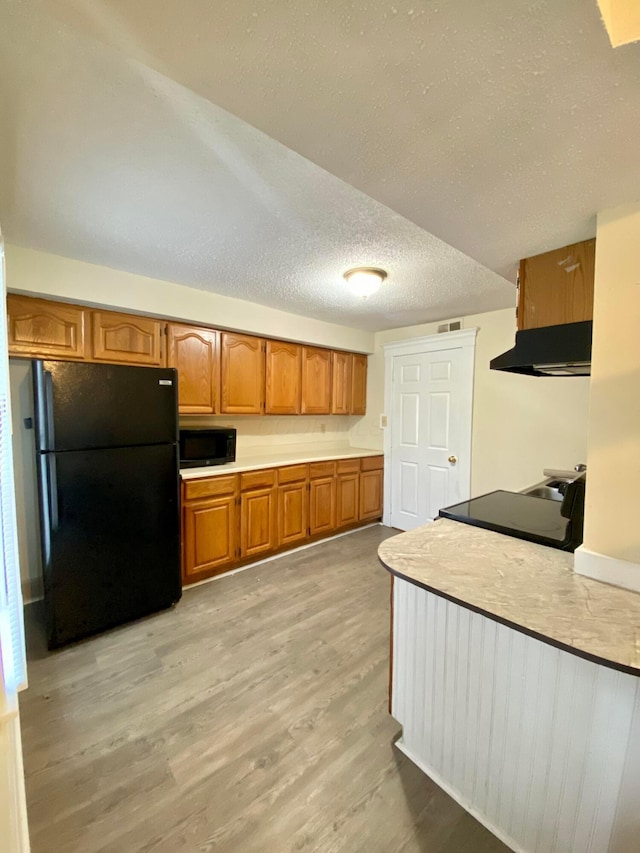 kitchen featuring a textured ceiling, light hardwood / wood-style floors, extractor fan, and black appliances