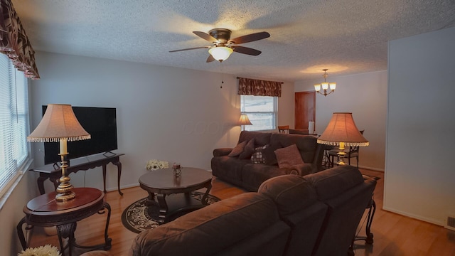 living room with a textured ceiling, light hardwood / wood-style floors, and ceiling fan with notable chandelier