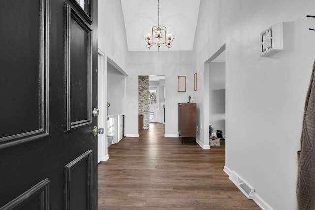 foyer entrance featuring dark wood-type flooring, high vaulted ceiling, and a chandelier