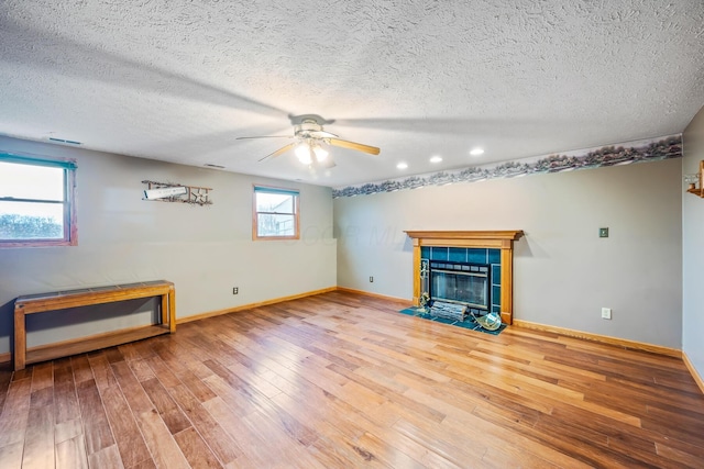 unfurnished living room featuring ceiling fan, a fireplace, wood-type flooring, and a textured ceiling