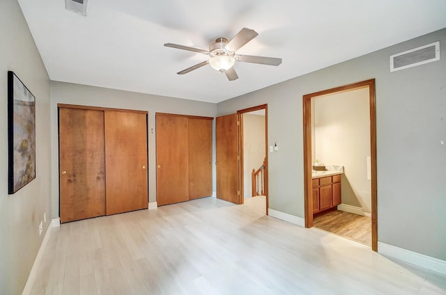 unfurnished bedroom featuring two closets, light wood-type flooring, ensuite bathroom, and ceiling fan