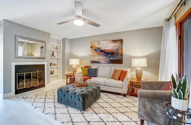 living room featuring built in shelves, light hardwood / wood-style floors, and ceiling fan