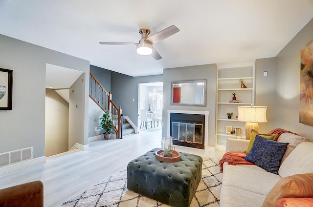 living room featuring light hardwood / wood-style floors, built in features, and ceiling fan