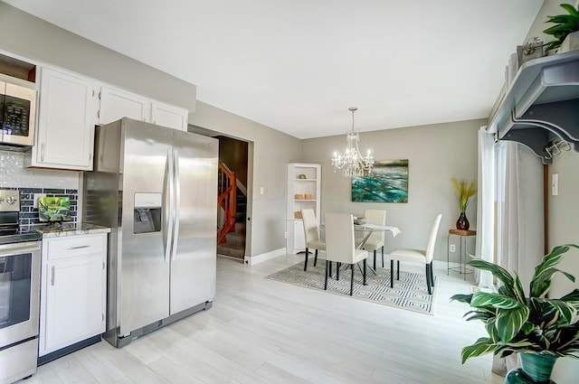 kitchen with white cabinets, hanging light fixtures, appliances with stainless steel finishes, tasteful backsplash, and a notable chandelier