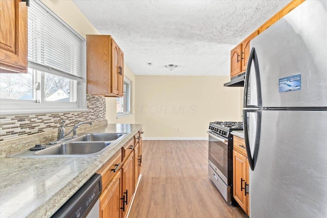 kitchen featuring sink, decorative backsplash, a textured ceiling, appliances with stainless steel finishes, and light hardwood / wood-style floors