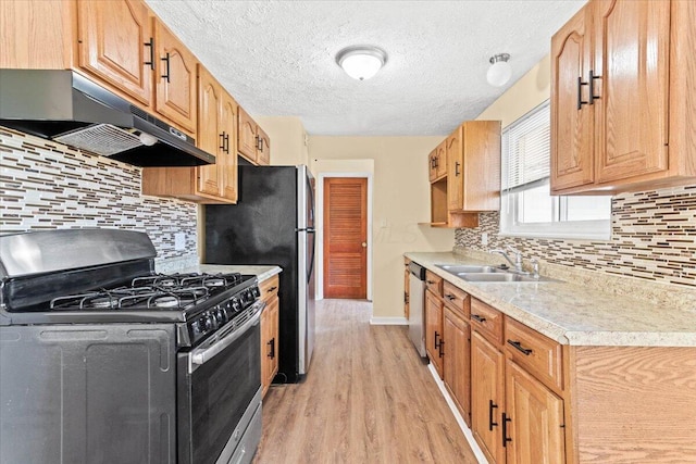 kitchen with sink, stainless steel appliances, light hardwood / wood-style floors, a textured ceiling, and decorative backsplash