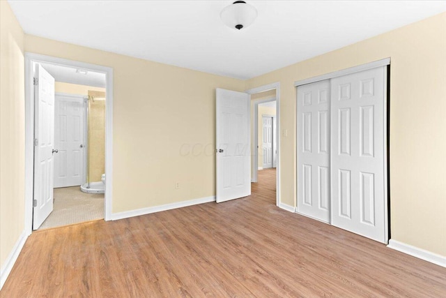 unfurnished bedroom with ensuite bathroom, a closet, and light hardwood / wood-style flooring