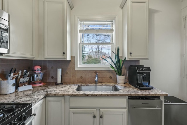 kitchen with light stone countertops, backsplash, stainless steel appliances, sink, and white cabinets