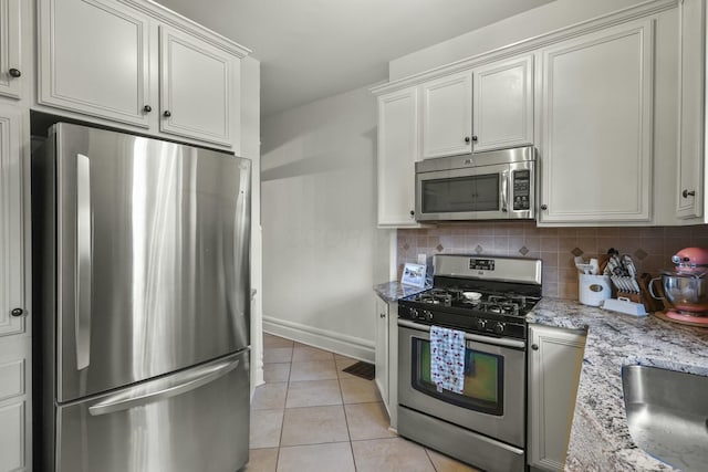 kitchen with light stone countertops, stainless steel appliances, light tile patterned floors, tasteful backsplash, and white cabinets