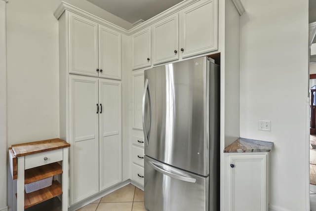 kitchen with white cabinets, stainless steel fridge, light tile patterned flooring, and dark stone counters