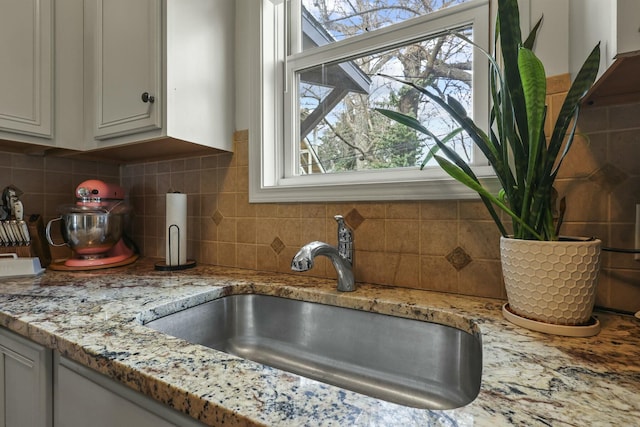 details with white cabinets, decorative backsplash, light stone counters, and sink