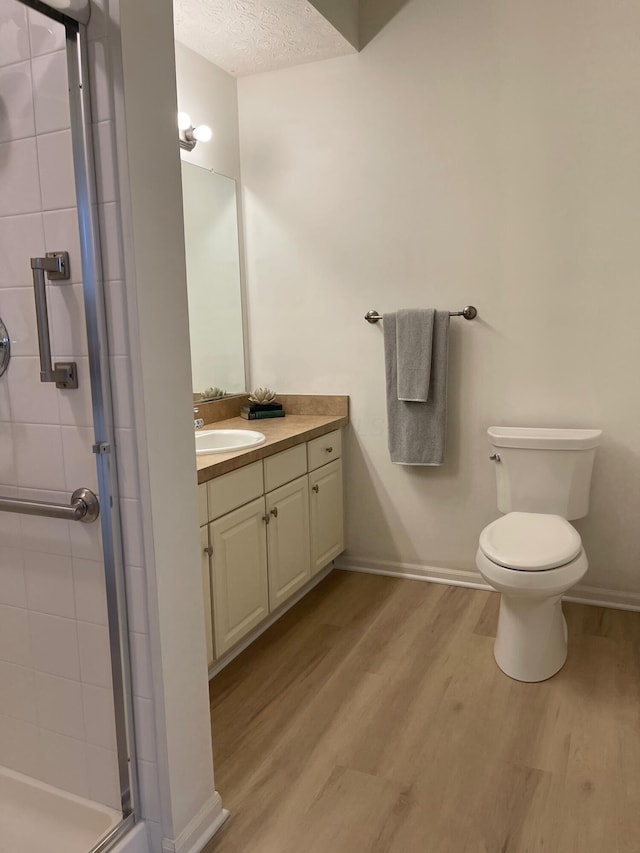 bathroom featuring walk in shower, vanity, a textured ceiling, hardwood / wood-style flooring, and toilet