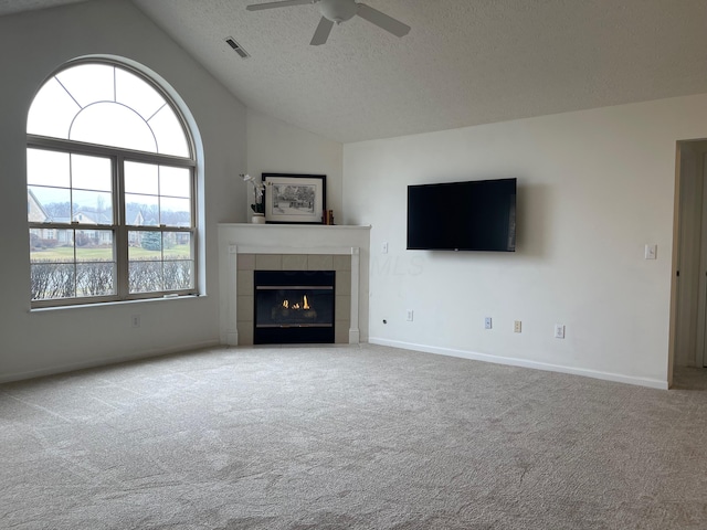 unfurnished living room with a tile fireplace, vaulted ceiling, ceiling fan, a textured ceiling, and light colored carpet