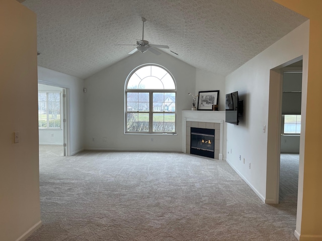 unfurnished living room featuring lofted ceiling, a textured ceiling, light colored carpet, a fireplace, and a ceiling fan