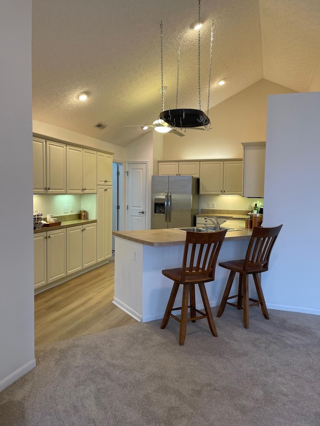 kitchen featuring a kitchen breakfast bar, stainless steel fridge with ice dispenser, kitchen peninsula, a textured ceiling, and lofted ceiling